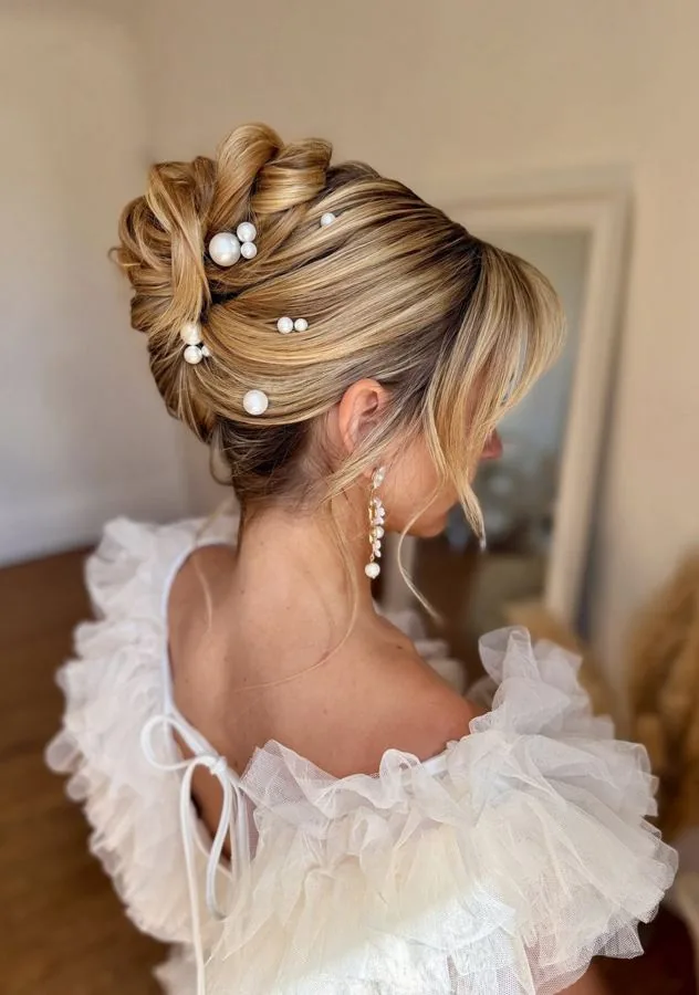 Chignon haut de mariée blond et texturé, semé de perles, qui tient toute la journée